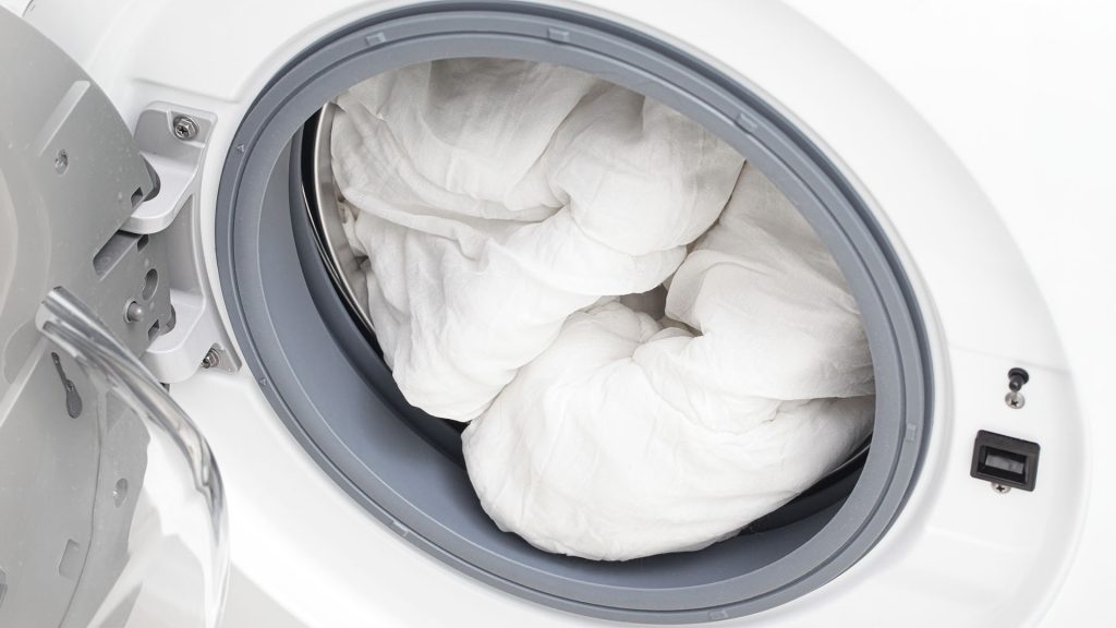 Comforter cleaning service with a white comforter placed inside a professional washing machine for deep cleaning and care.